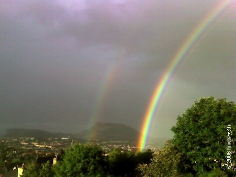 primary and secondary rainbow over town and hill