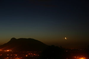 small lunar crescent rising next to nocturnal hill